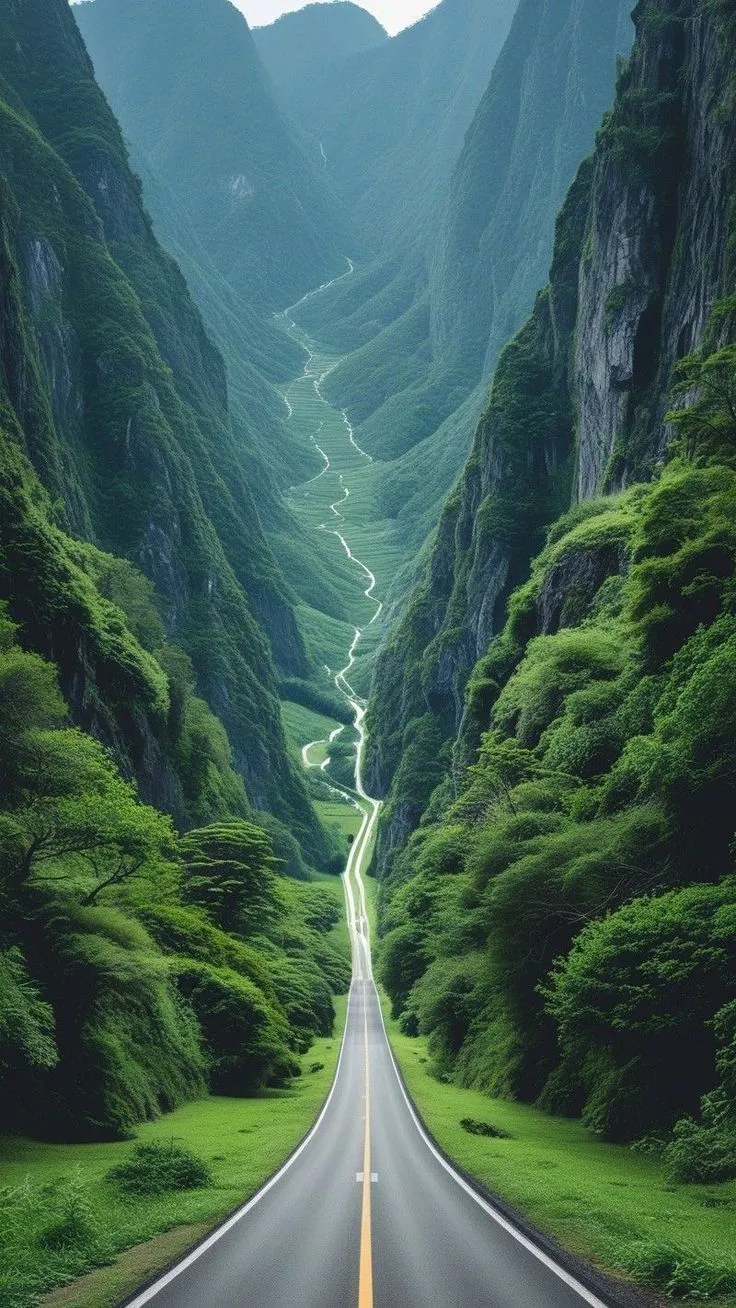 an empty road in the middle of a mountain range with green grass on both sides