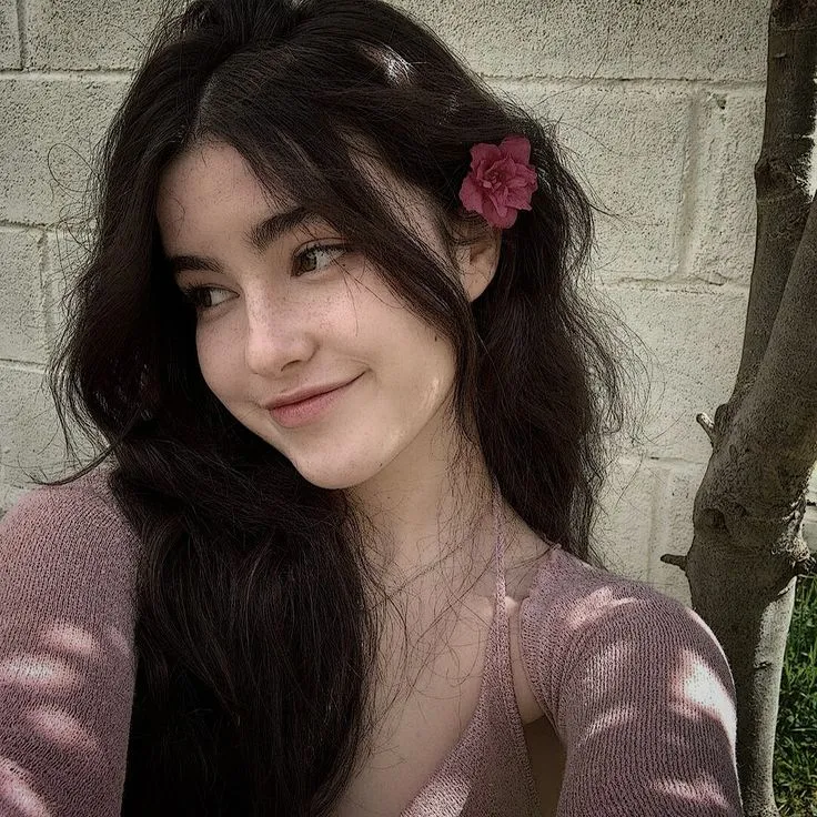 a woman with long hair and a pink flower in her hair smiles at the camera