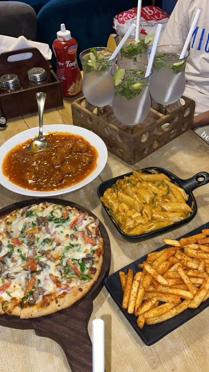 pizza, french fries and other foods on a table at a restaurant with people sitting around