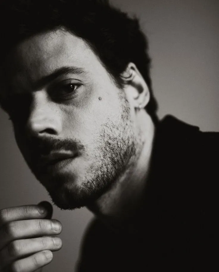 a black and white photo of a man with his hand on his chin looking at the camera