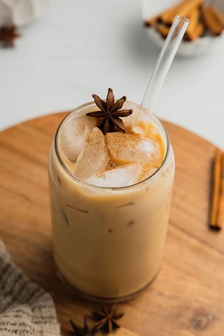 an iced drink on a wooden tray with cinnamon sticks and star anisette garnish