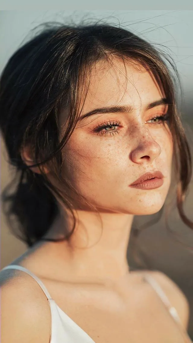 a woman with freckled hair wearing a white top and looking off into the distance