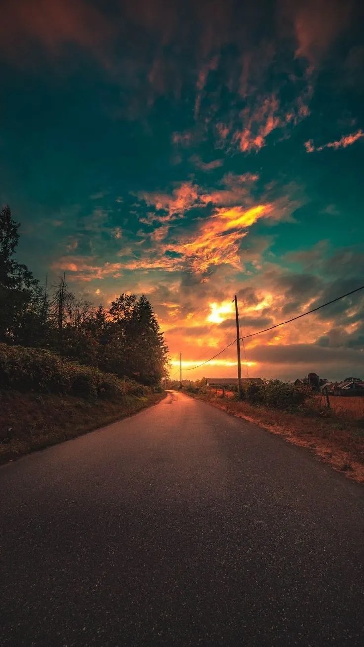 the sun is setting over an empty road