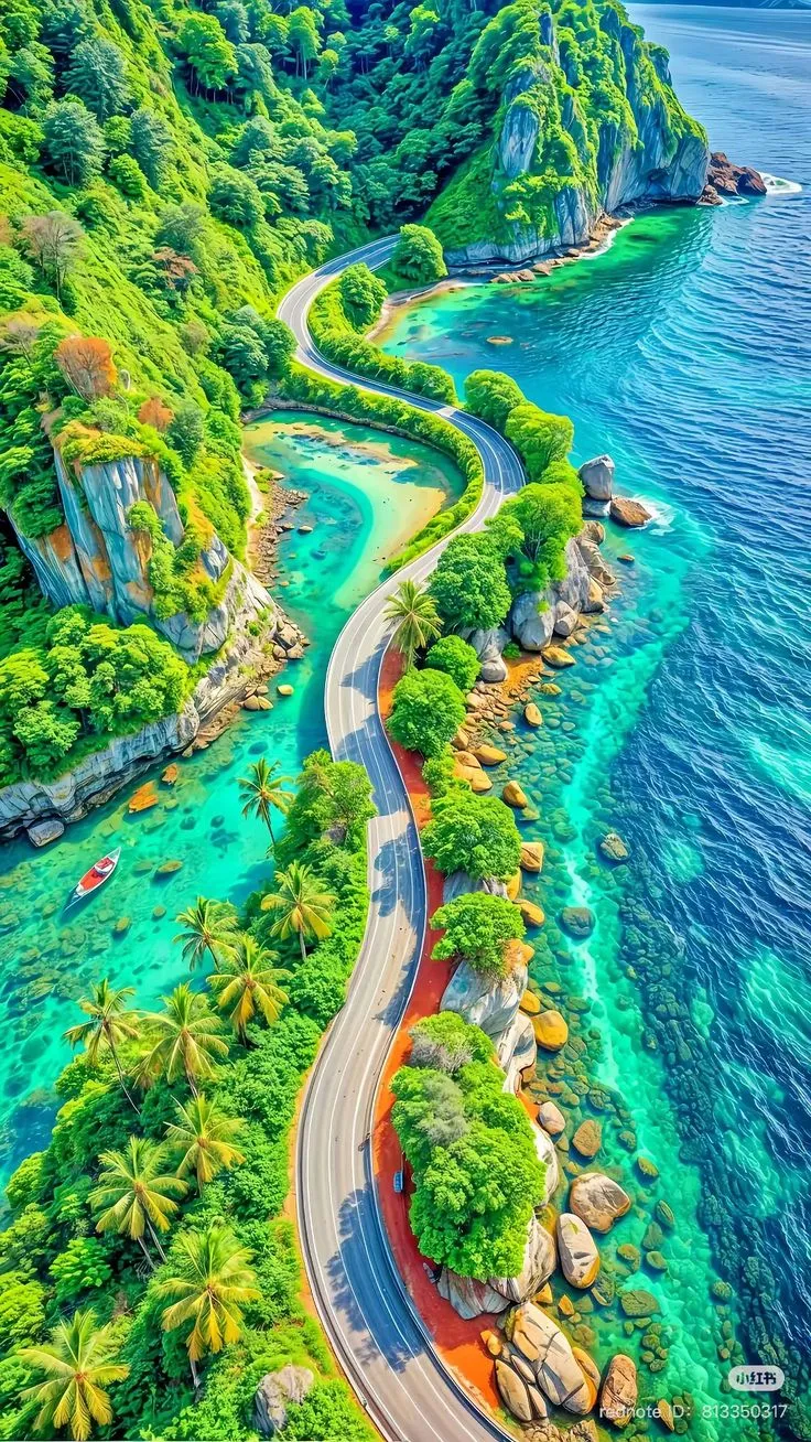 an aerial view of a winding road in the middle of blue water with green trees on both sides