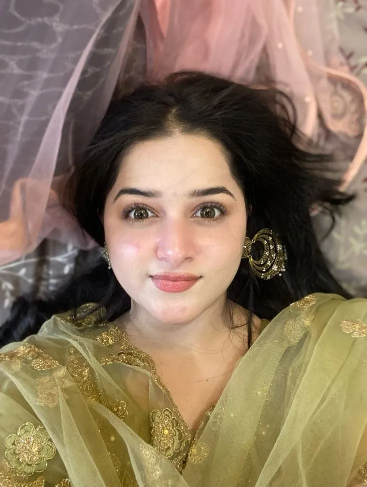 a woman with long black hair wearing a green sari and gold earrings on her head