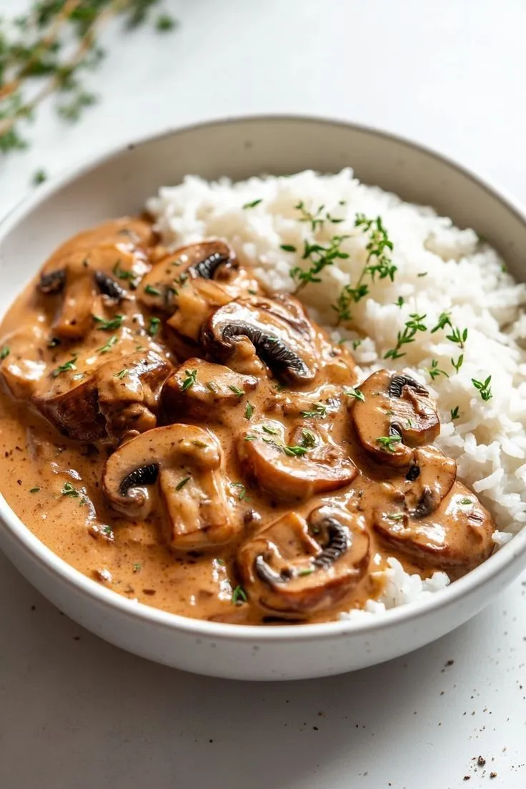 a bowl filled with rice and mushrooms on top of a white tablecloth next to a fork