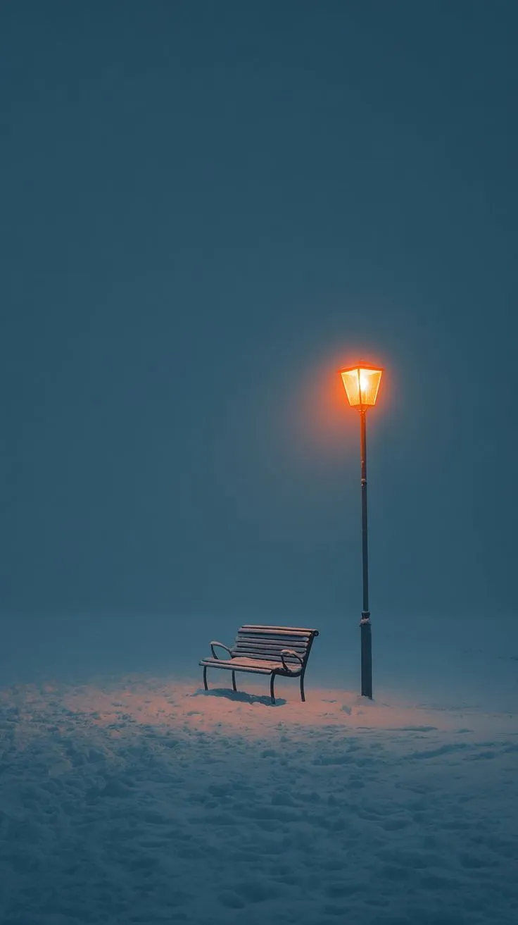 a park bench sitting under a street light in the middle of snow covered ground at night