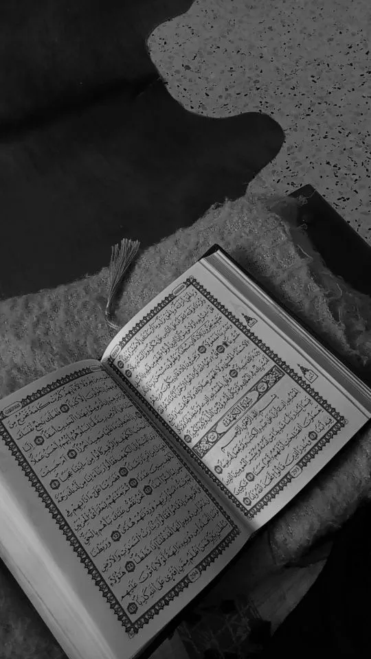 an open book sitting on top of a bed next to a black and white photo