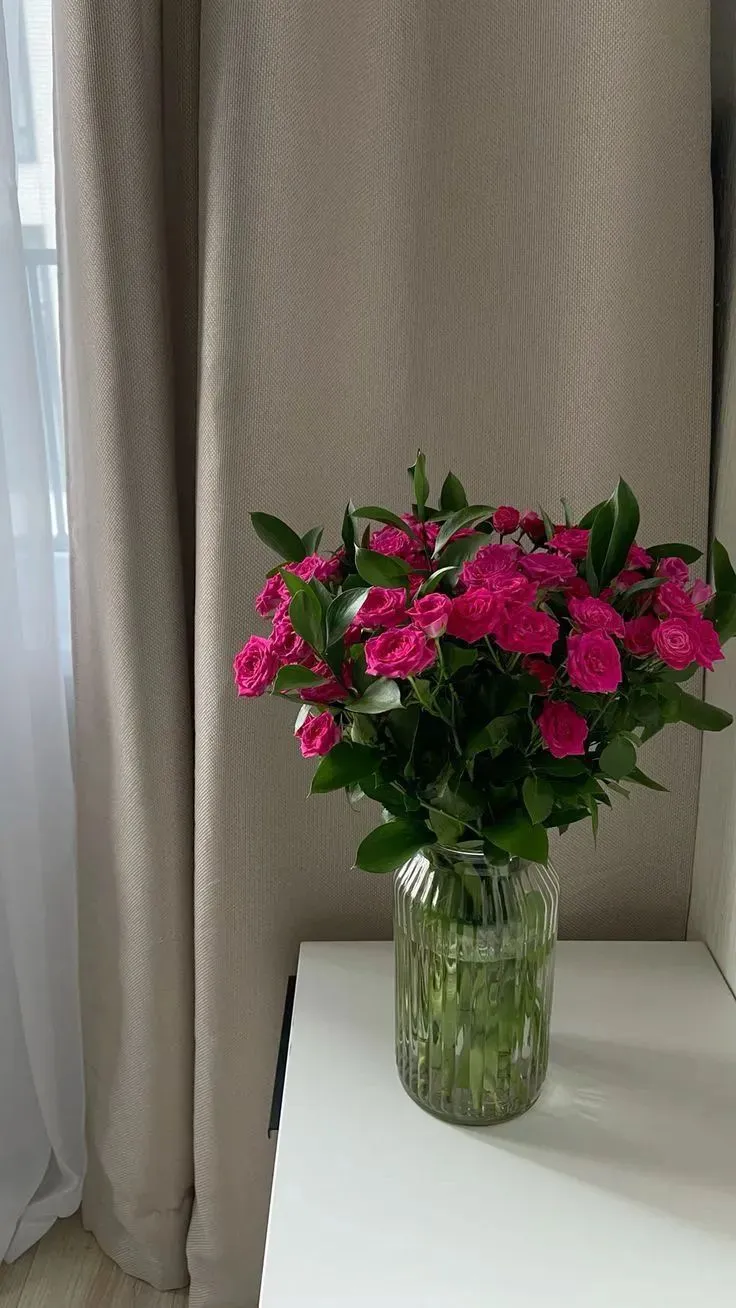 a vase filled with pink flowers sitting on top of a white table next to a window