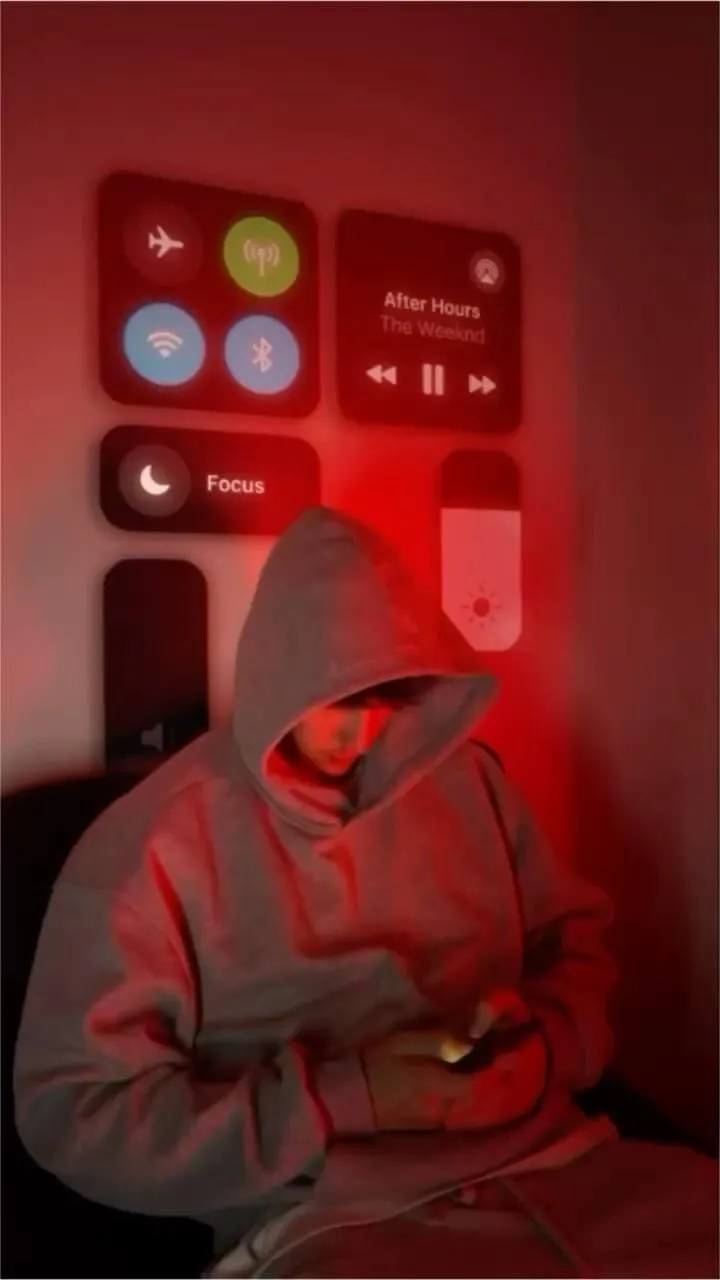 a person in a hoodie using a cell phone with red light coming from the screen