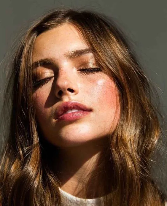 a woman with her eyes closed and long hair in the wind, wearing a white sweater