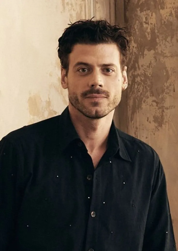 a man standing in front of a wall wearing a black shirt