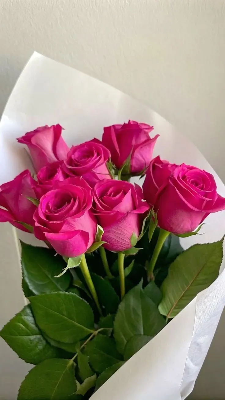 a bouquet of pink roses sitting on top of a white paper wrapped in wax paper
