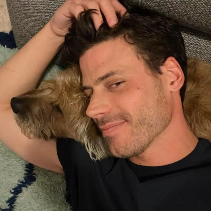 a man laying on top of a couch next to a brown dog wearing a black shirt