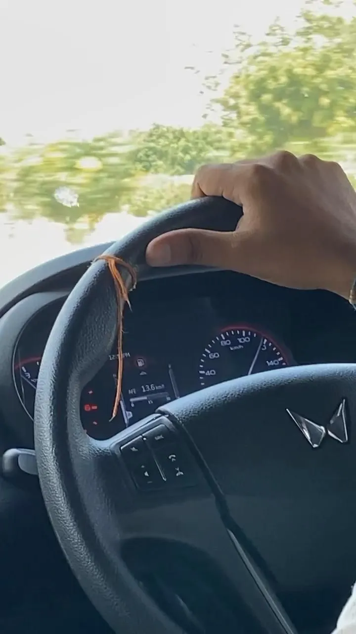 a person driving a car with their hand on the steering wheel while holding onto an orange string
