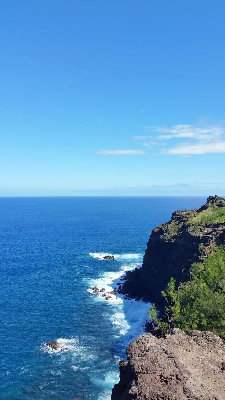 the ocean is blue with waves coming in from the shore and green trees on the cliff