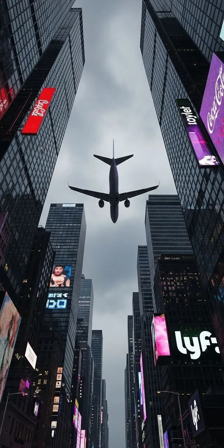 an airplane is flying through the air over some buildings and billboards in new york city