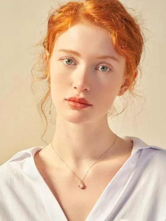 a young woman with red hair wearing a white shirt and holding a necklace on her neck