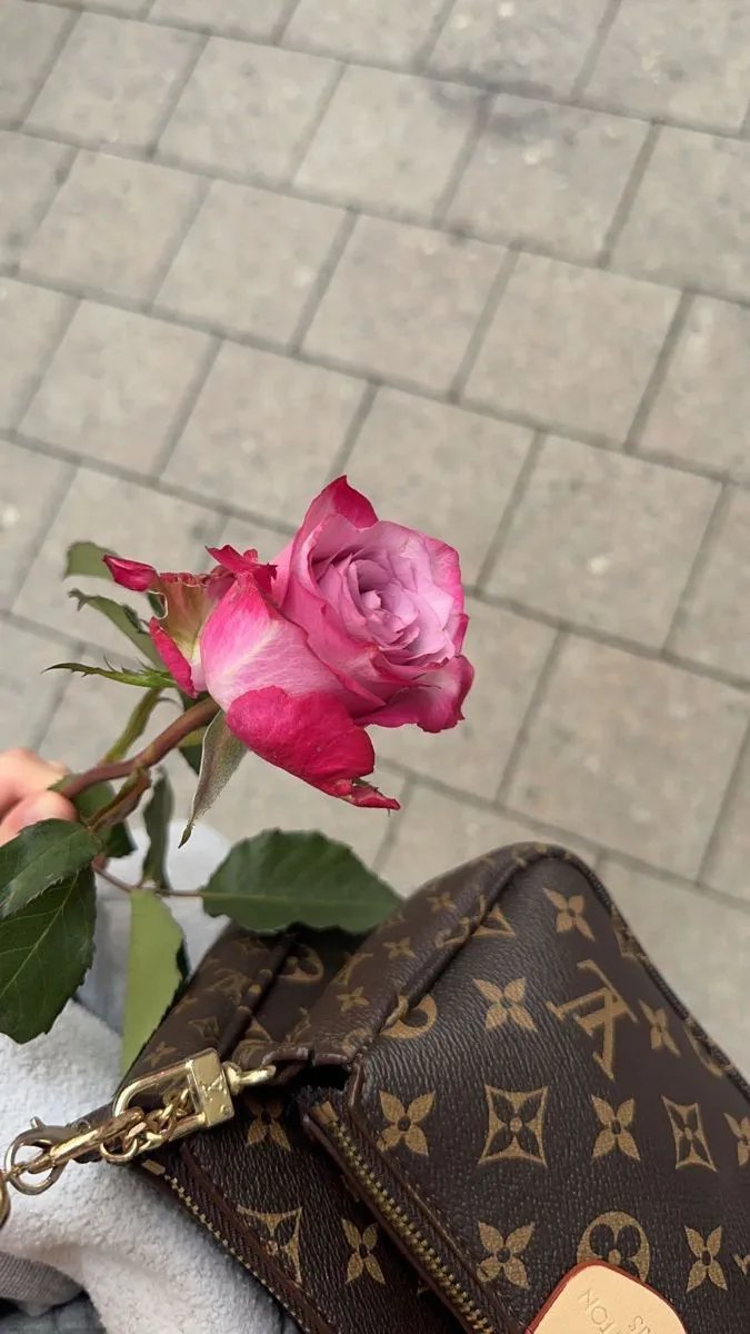 a pink rose sitting on top of a purse next to a person's hand