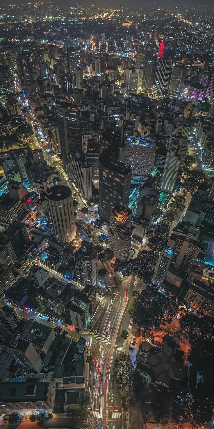 an aerial view of a city at night with lots of lights and buildings in the foreground