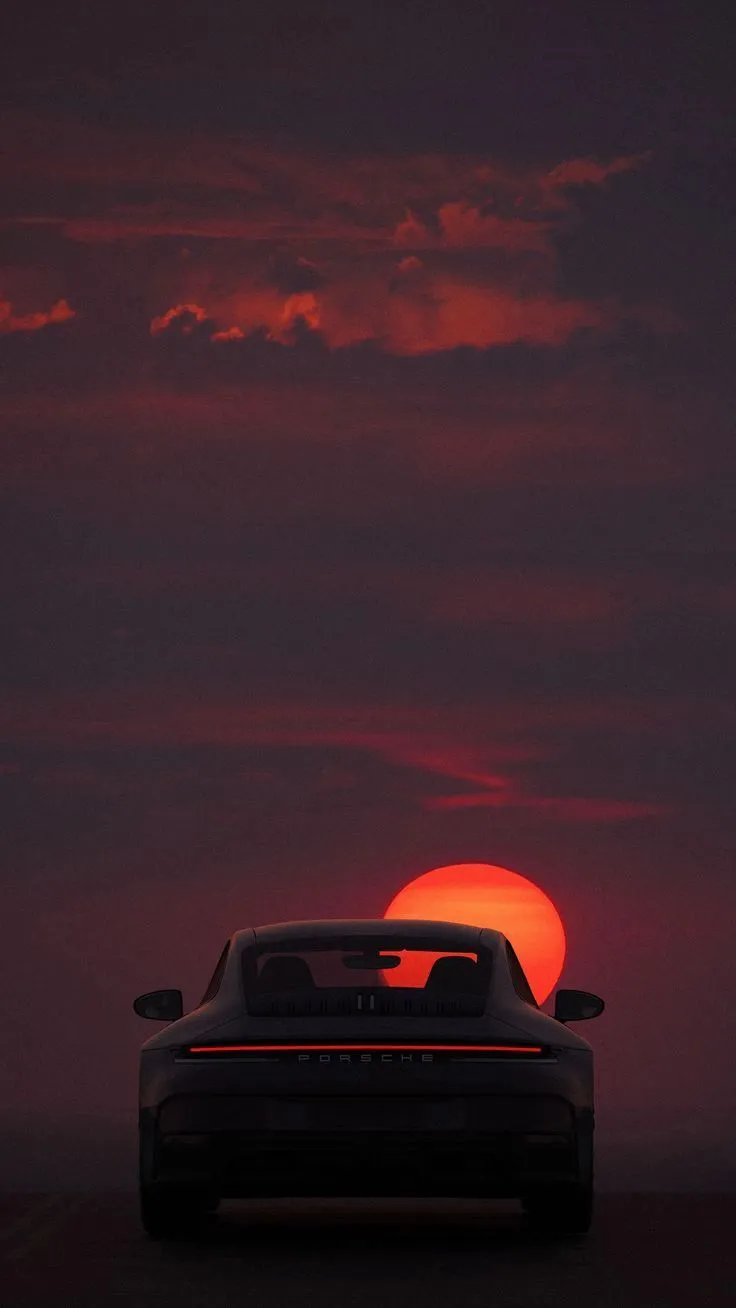 the back end of a car in front of a setting sun with clouds above it