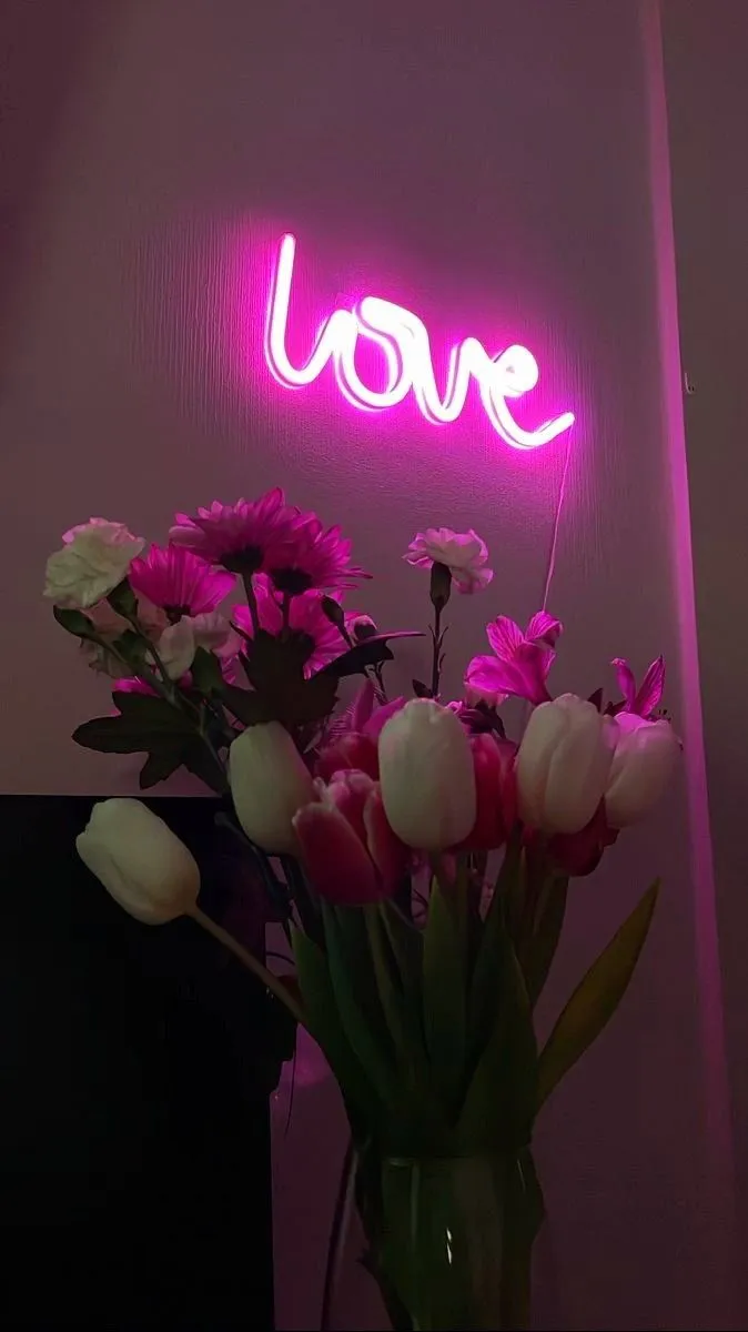 a vase filled with pink flowers next to a neon sign that says love on the wall