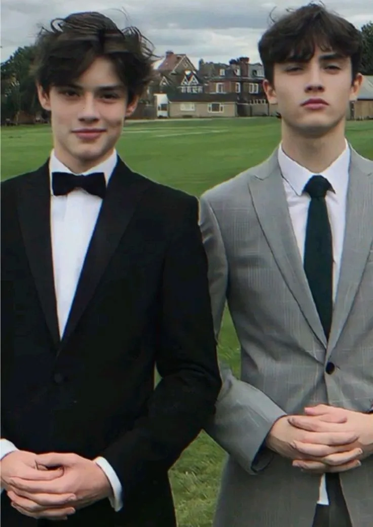 two young men wearing suits and ties standing next to each other in front of a field