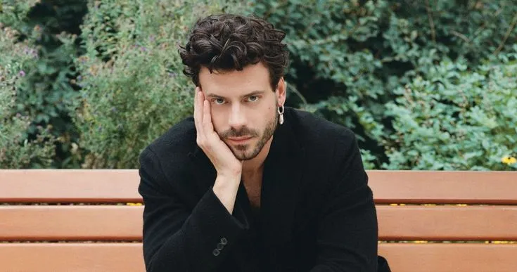 a man is sitting on a bench with his hand under his chin and looking at the camera