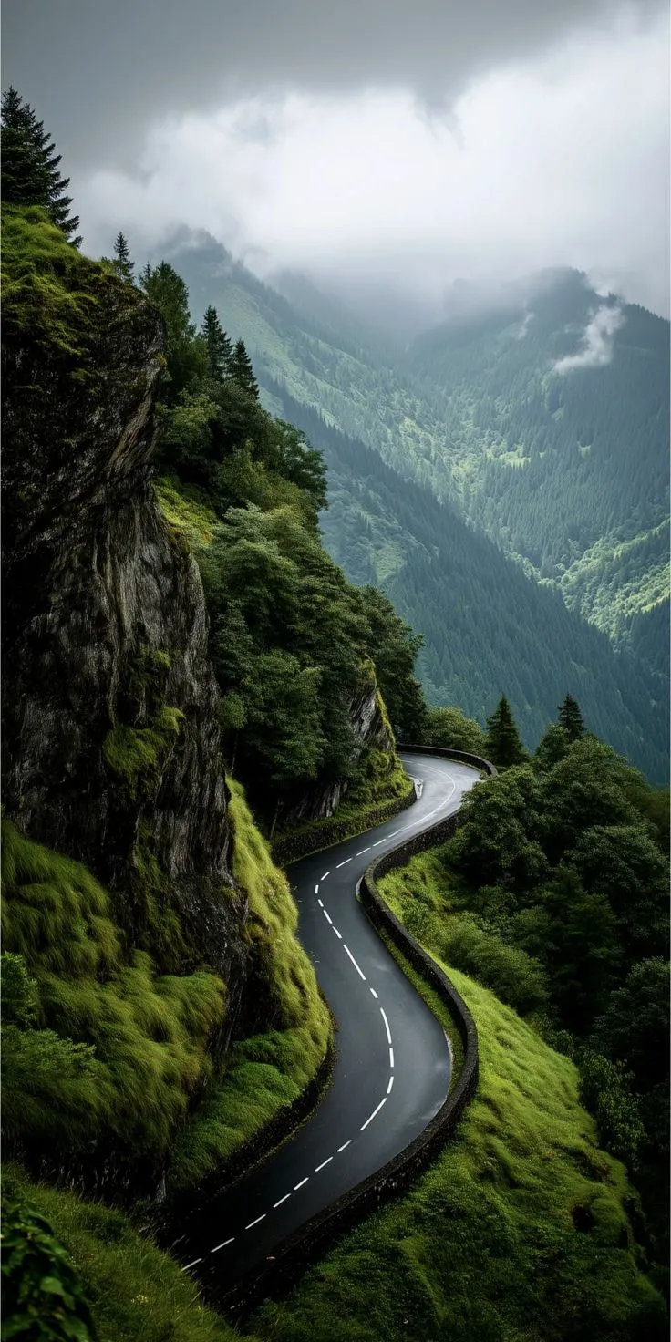a winding road in the middle of a lush green mountain range under a cloudy sky