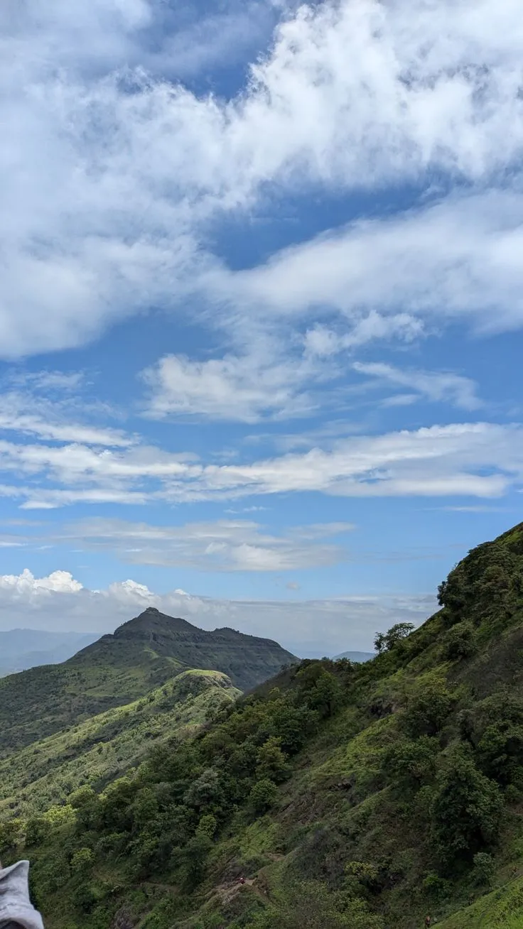 a man riding a horse on top of a lush green hillside under a cloudy blue sky
