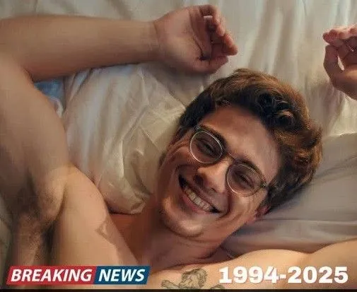 a man laying in bed wearing glasses and smiling for the camera with his hands up
