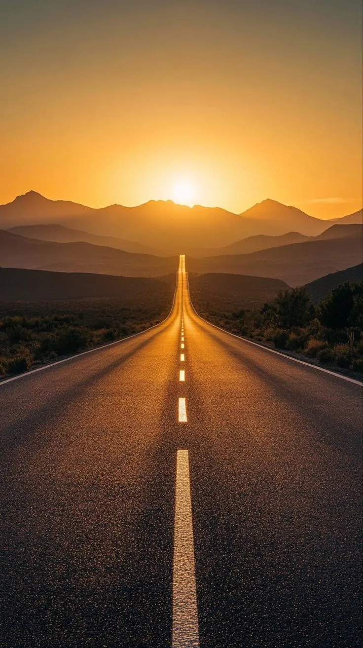 the sun is setting on an empty road in the middle of nowhere, with mountains in the distance