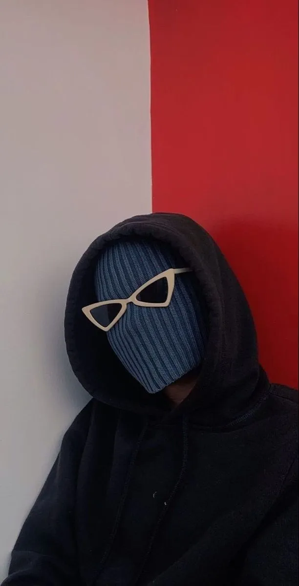 a person wearing a hoodie with sunglasses on their face, sitting against a red and white wall