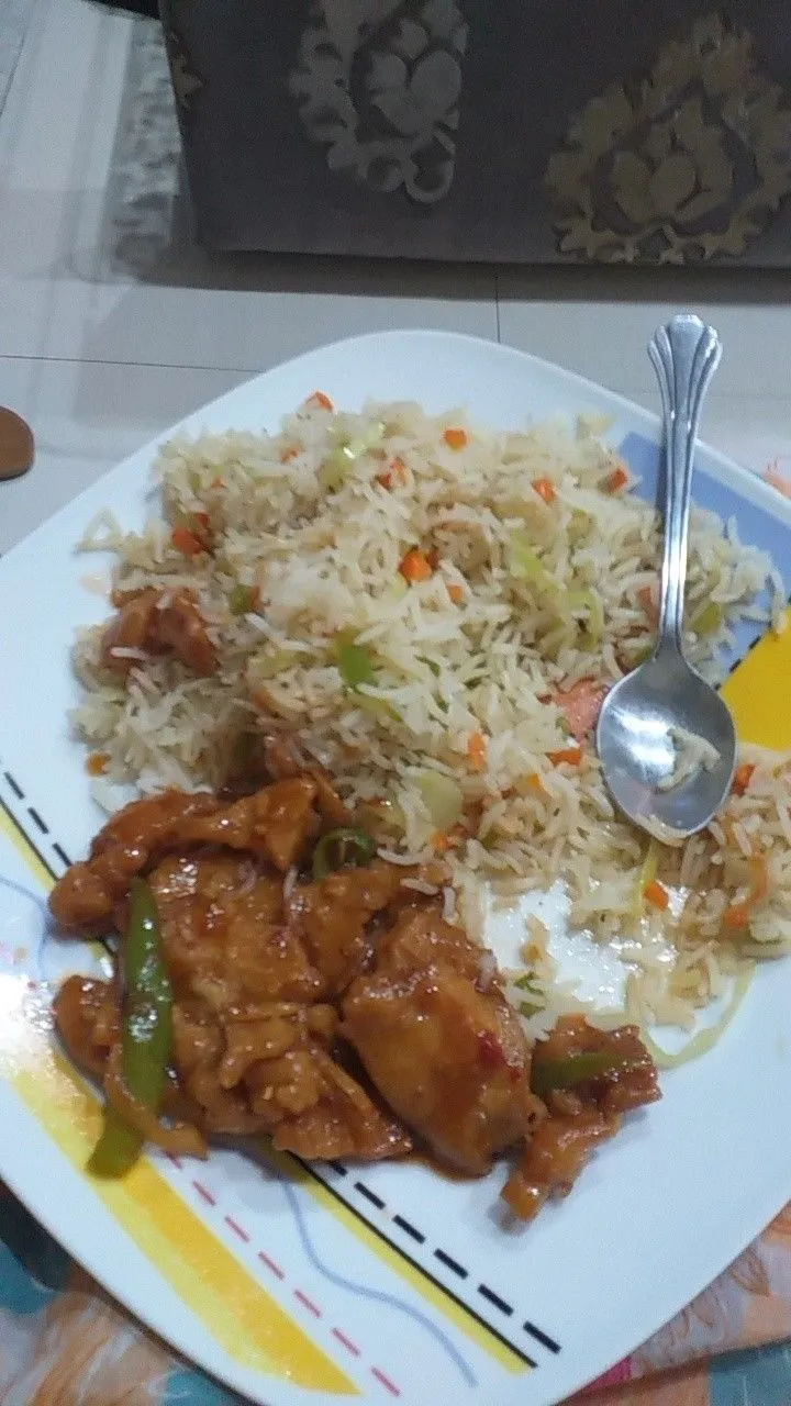 a white plate topped with rice and meat next to a spoon on top of a table