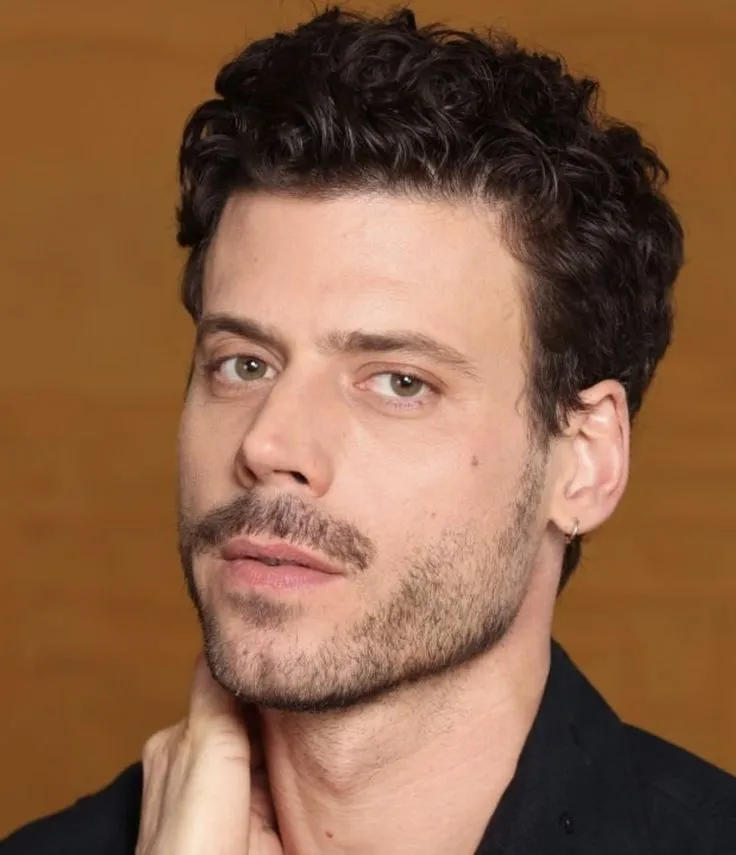 a close up of a person wearing a black shirt and holding his hand to his chin
