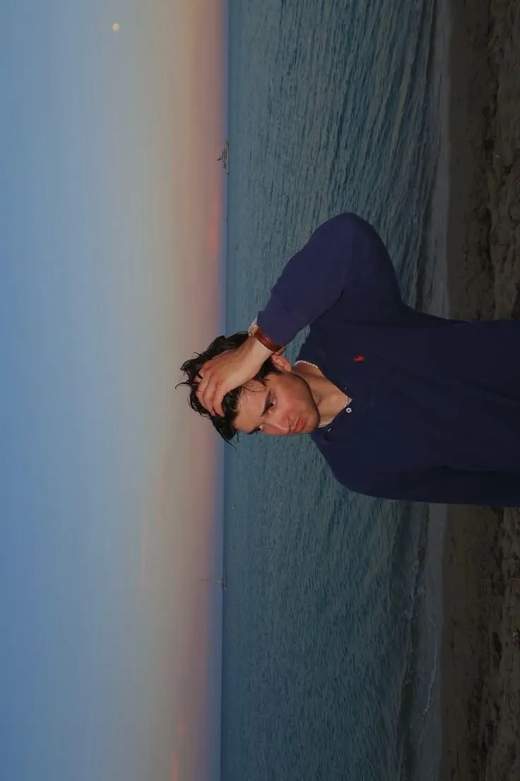 a man standing next to the ocean with his hand on his head