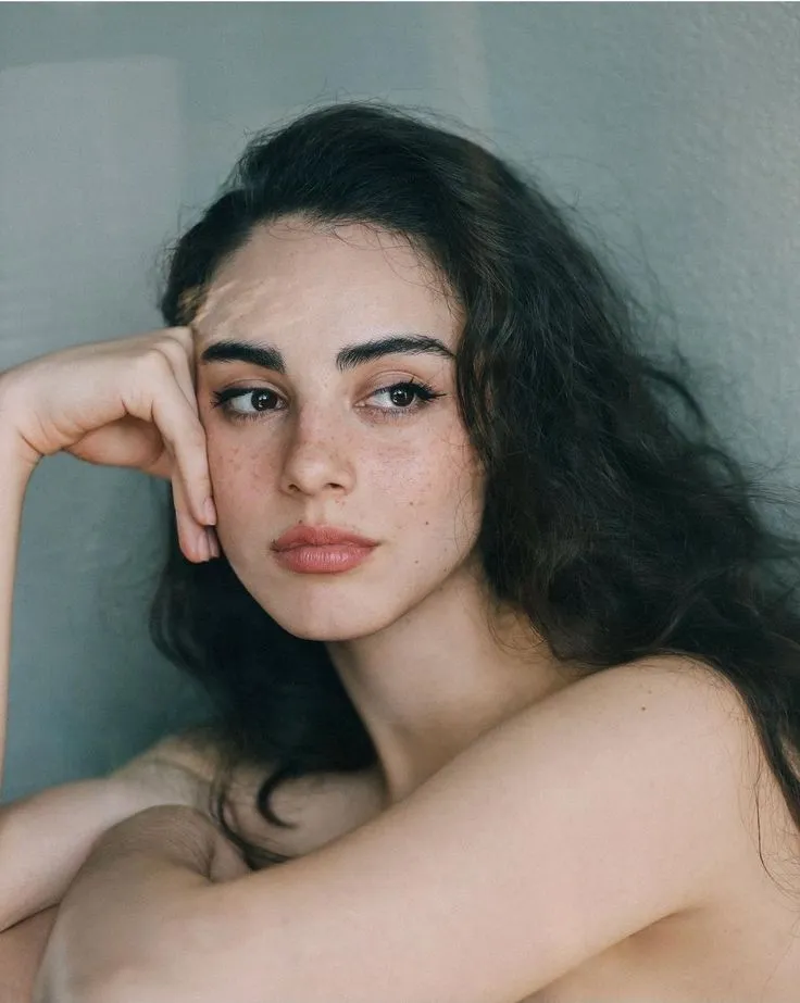 a woman with long dark hair is posing for the camera and has her hand on her head
