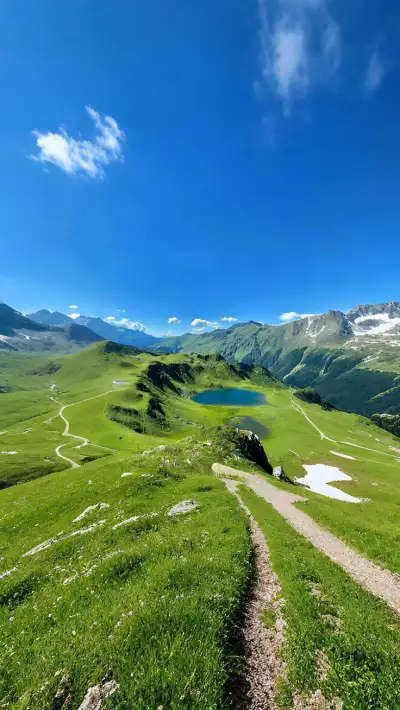 a trail winds through the grass towards a body of water in the distance, surrounded by mountains