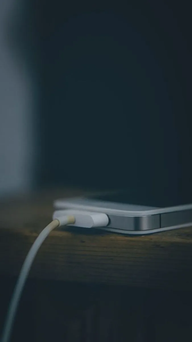 an iphone plugged in to a charger on a wooden table with dark background