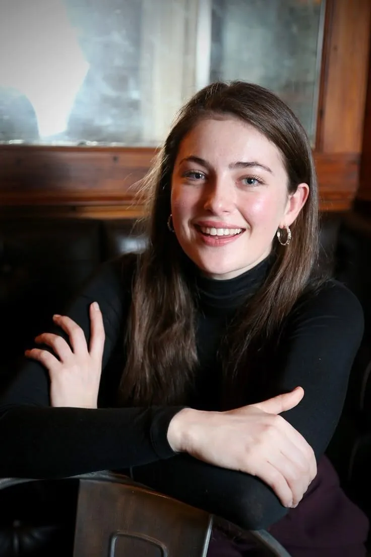a woman sitting at a table with her arms crossed and looking into the camera smiling