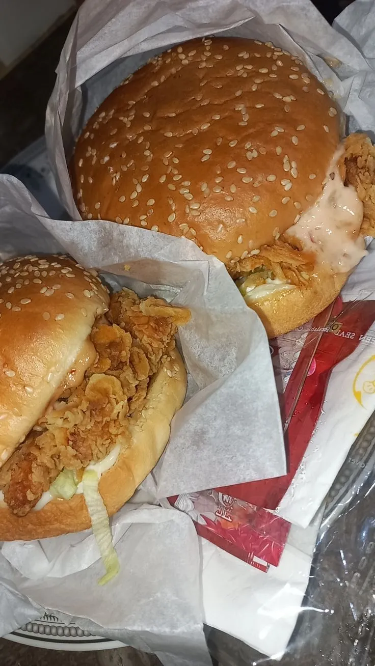two chicken sandwiches sitting on top of wax paper wrapped in plastic wrappers next to each other