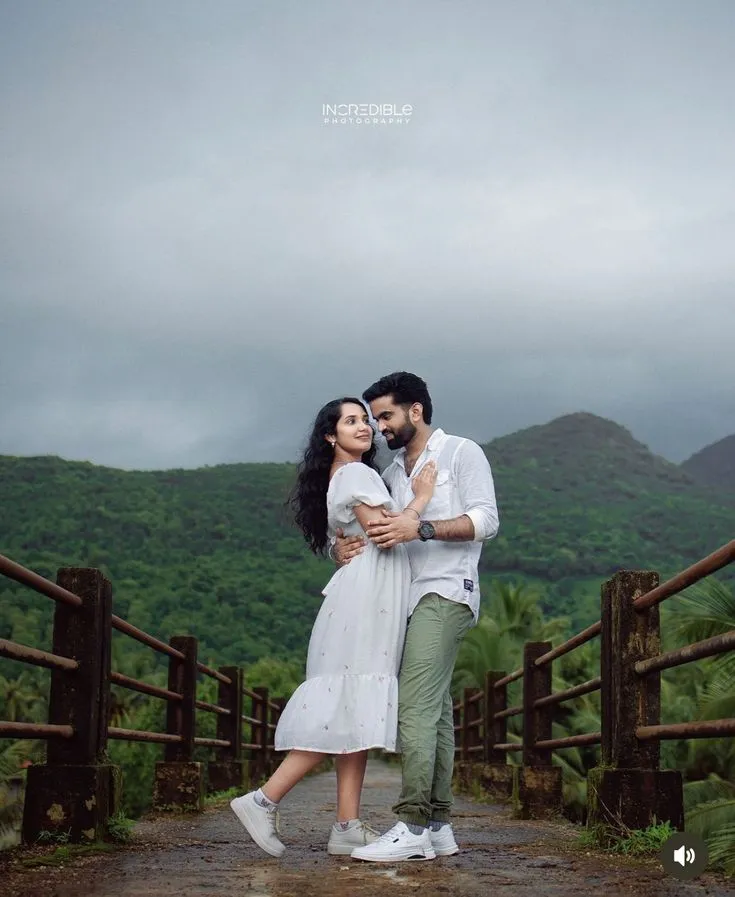 a man and woman standing on a bridge with mountains in the background