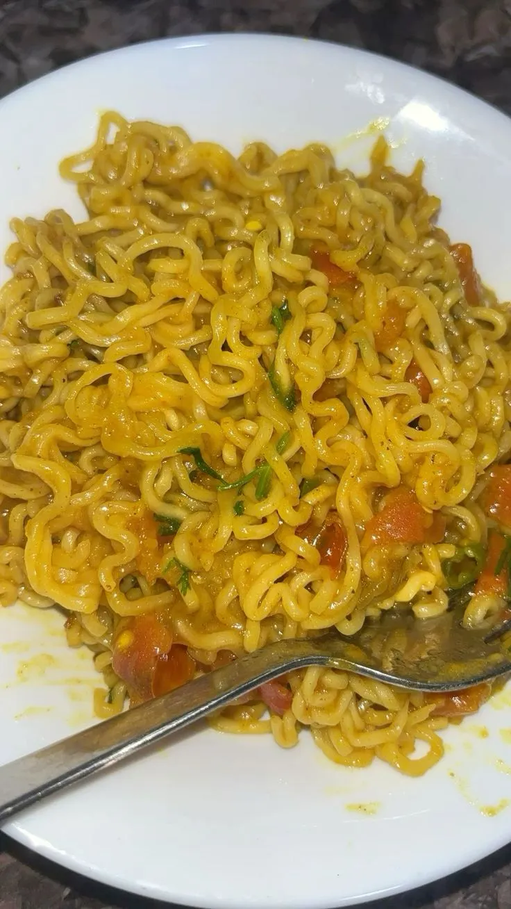 a white plate topped with noodles and vegetables next to a fork on top of a table