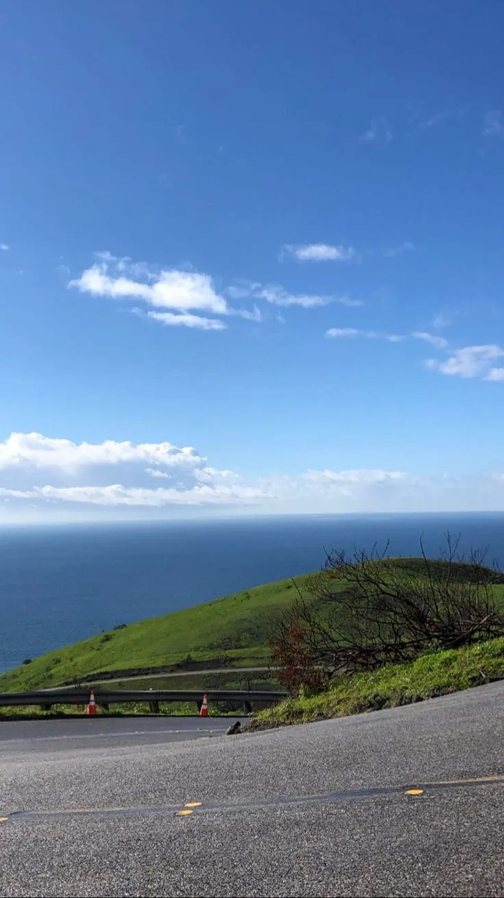 a stop sign on the side of a road next to an ocean and grassy hill