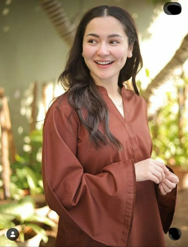 a woman in a brown dress smiling at the camera with her hands on her hips