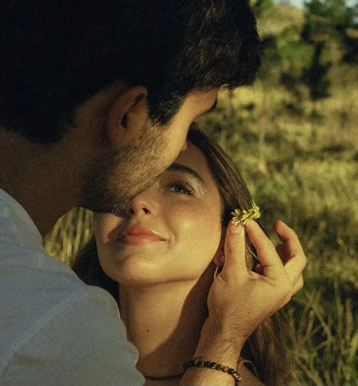 a man and woman standing next to each other in the grass with their eyes closed