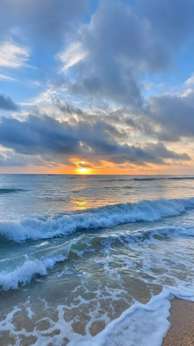 the sun is setting over the ocean with waves coming in to shore and some clouds