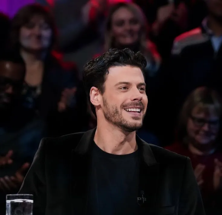 a smiling man sitting in front of a crowd
