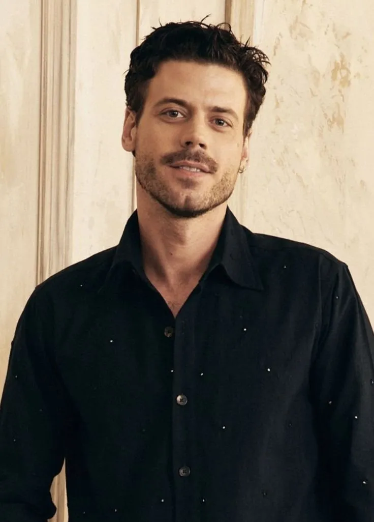 a man standing in front of a wall wearing a black shirt
