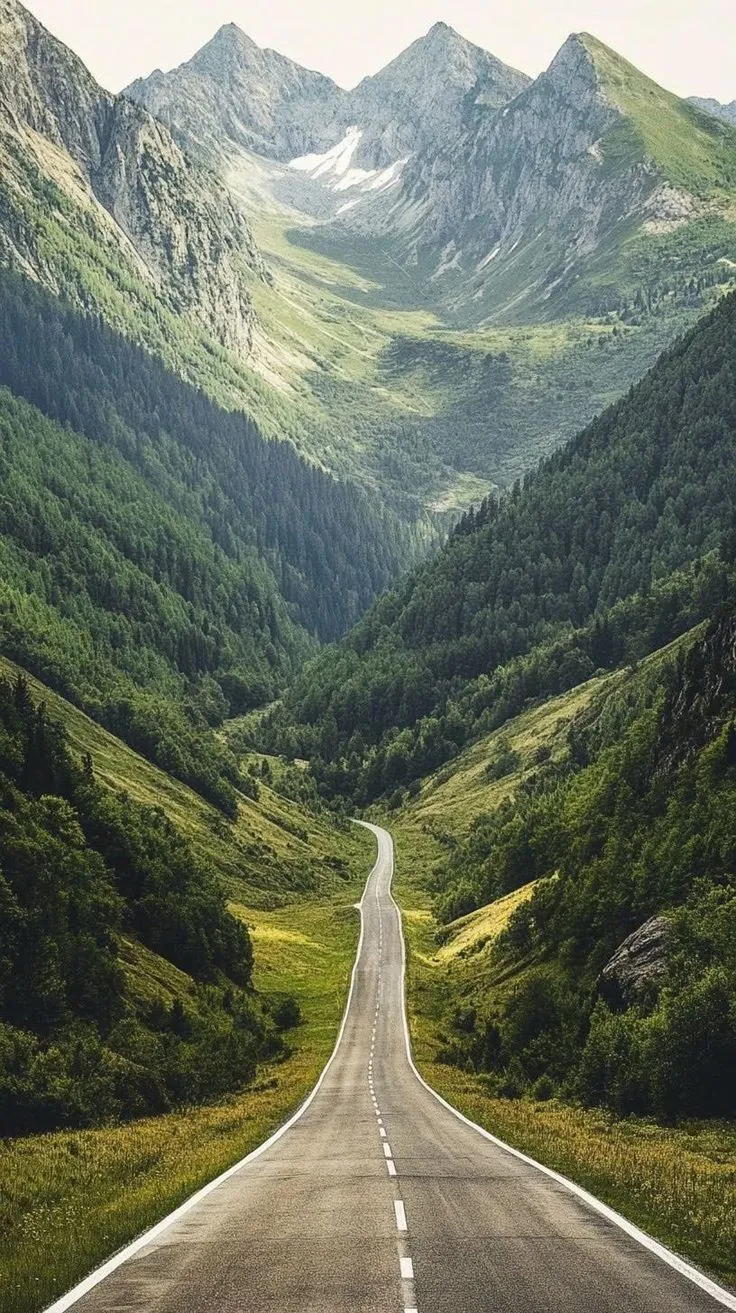 an empty road in the middle of a mountain range with green grass and trees on both sides